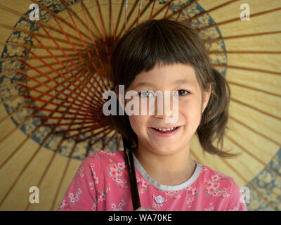 Cute mixed-race little girl (Caucasian and Southeast Asian) smiles under her traditional Chinese oil-paper parasol. Stock Photo