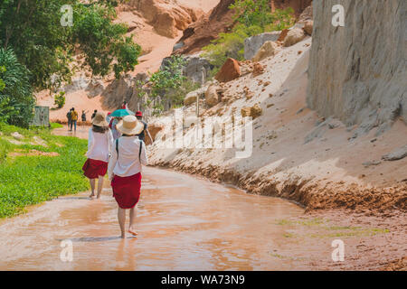 Back view of tourists walk on feet in the Red Stream ( it also named Fairy Stream) with Beautiful scenic landscape with red river, sand dunes and jung Stock Photo