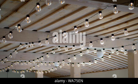 Warm color string light bulbs pending on a wooden rustic ceiling Stock Photo