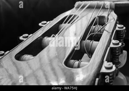 Headstock of an acoustic guitar. Details of the head with the nylon strings coiled on the tuning pegs of an old acoustic guitar, worn out and dusty. B Stock Photo