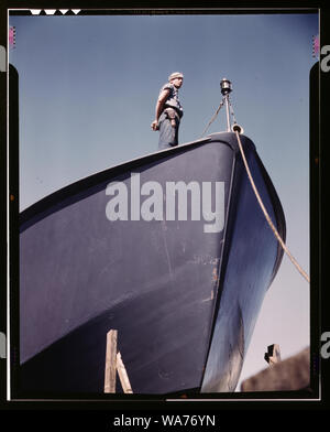 A Coast Guard sentry stands watch over a new torpedo boat under construction at a southern shipyard. In addition to wooden torpedo boats, the yard also turns out many steel boats for the Navy. Higgins Industries, Inc., New Orleans, La. Stock Photo