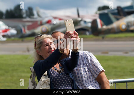 Biggin Hill, UK. 18 August 2019. A lady takes a photo with her mobile phone as the Biggin Hill Festival of Flight continued for a second day. The world-famous Festival of Flight at London Biggin Hill Airport had awe inspiring displays. Taking part were RAF Typhoon Jet Fighters, Breitling Jet Team and the Battle of Britain Memorial Flight. Twelve multi aircraft teams with a total of 49 aircraft took to the skies at London’s only air show. Credit: Keith Larby/Alamy Live News Stock Photo