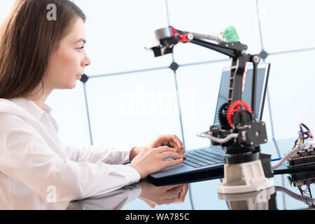 A young woman writes an algorithm for the robot arm. Science Research Laboratory for Robotic Arm Model. Computer Laboratory Stock Photo