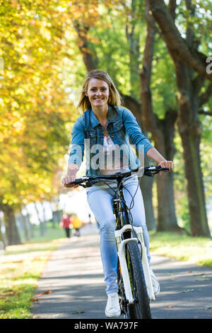 Young woman ride bike in autumn park. Enjoying while cycling in nature during autumn day. Stock Photo