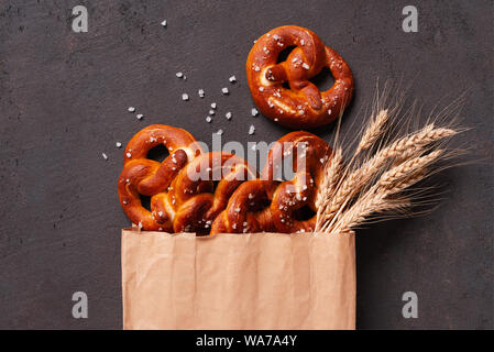 Fresh salted pretzels in the paper bag on the brown table decorated with wheat ears, top view composition Stock Photo