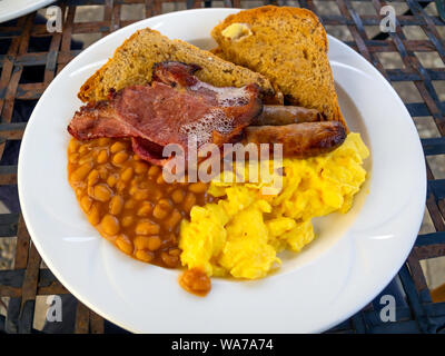 English farmhouse eaten outdoors Breakfast bacon scrambled egg sausages baked beans with brown granary buttered toast Stock Photo