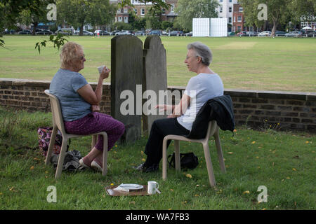 Afternoon tea UK  People two women friends catching up, chatting over a cup of English tea sitting in a church graveyard London, England 2019  2010s HOMER SYKES Stock Photo