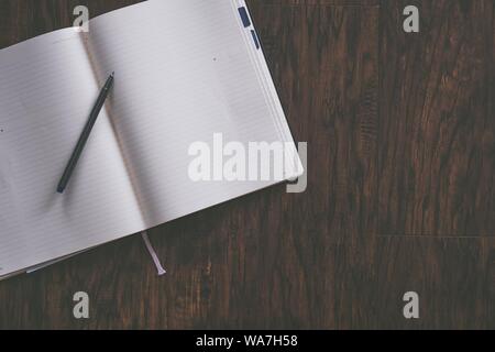 Overhead shot of an opened textbook with a ballpoint pen on it on a brown wooden background Stock Photo