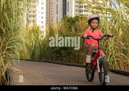 Little girl riding bicycles along a wooden path outside the city wearing helmets as protective equipment Stock Photo