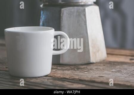 Closeup shot of a white ceramic cup next to a stainless metal kettle on a wooden surface Stock Photo