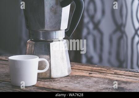 Closeup shot of a white ceramic cup next to a stainless metal kettle on a wooden surface Stock Photo