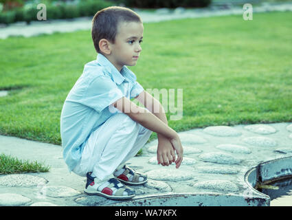 A sad boy is sitting on the street alone. Unhappy lonely child. Blue tone Stock Photo