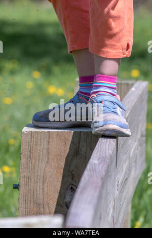 A young girl walks on top of a fence in colorful sneakers, as she balances on this tall wood beam Stock Photo