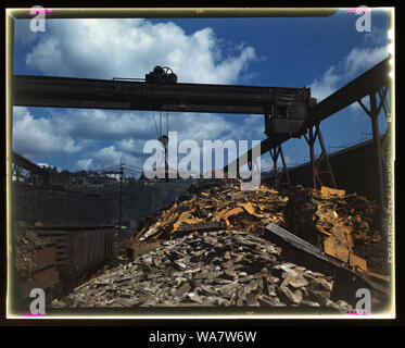 Back into production go these carloads of scrap metal, Allegheny Ludlum Steel[e] Corp., Brackenridge, Pa. The melting of alloy steels for defense work requires that steel mill scrapyards such as this be constantly filled. The overhead magnet deposits the scrap in a loader which carries it to the open-hearth furnace. About 50 per cent scrap steel is used in open-hearth production Stock Photo