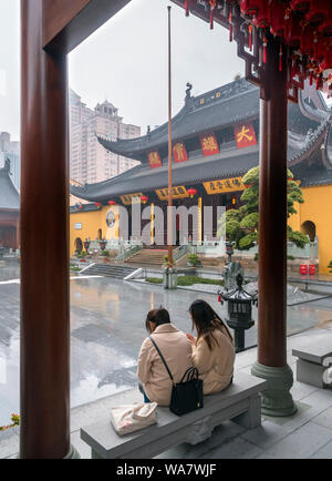 Shanghai, China. Two young women sheltering from the rain in front of the Grand Hall at the Jade Buddha Temple, Shanghai, China Stock Photo