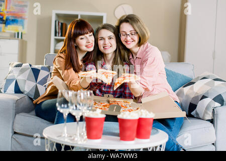 Group of three young girls friends eating pizza during party at home. Group of young women having fun together. Happy women talking and laughing while Stock Photo