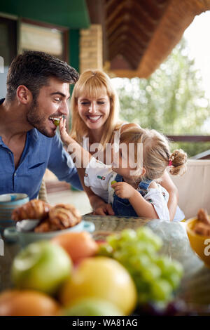 Cute little girl feeds her father with grape for breakfast Stock Photo