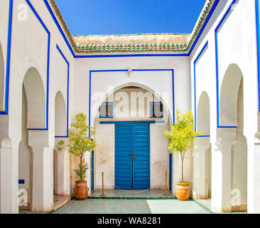 Courtyard at El Bahia Palace, Marrakech, Morocco. there are white walls and columns with blue signs and blue doors.