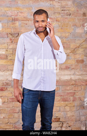 A serious handsome young man talking on his phone in a white shirt. Stock Photo