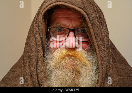 Elderly man wearing hooded blanket to keep warm Stock Photo