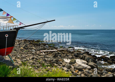 Rocky shore over the beautiful Black Sea, in Nessebar, Bulgaria. In the background a sky with clouds.The front of the ship is visible on the shore. Stock Photo