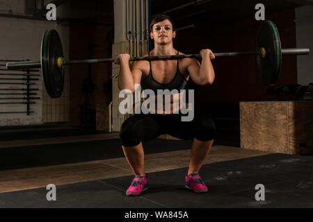 A  short haired woman with muscles is doing weight lifting with a barbell in a gym. The athletic young woman is doing front squats Stock Photo