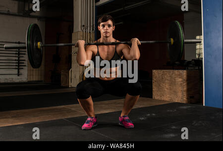 A muscular short haired woman with Sixpack is doing weight lifting with a barbell in a gym. The athletic woman is doing front squats. Stock Photo