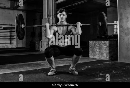 A fit short haired woman with Sixpack is doing weight lifting with a barbell in a gym. The muscular woman is doing front squats. Stock Photo