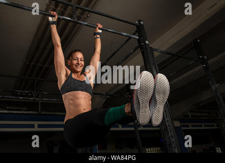A sporty woman is doing a fitness workout and having fun.The muscular and attractive woman is doing the exercise l sit on the horizontal bar. Stock Photo