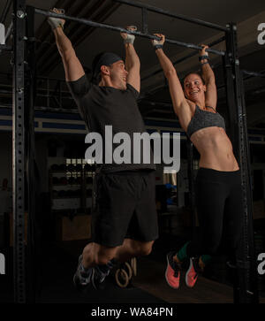 An athletic couple is doing a fitness workout together and having fun.The muscular and attractive man and woman are doing the exercise toes to bar.v Stock Photo