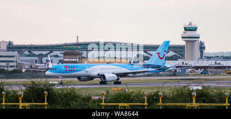 A Tui Airways Boeing 757-200 plane turns off the runway in front of the air traffic control tower and the Gatwick Pier 6 Bridge Stock Photo