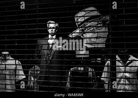 Mannequin in a fancy double breasted pinstripe suit in a window display behind bars at night Stock Photo