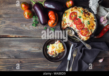 Fresh homemade moussaka in iron skillet on rustic wooden background with ingredients. Top view. Greek cuisine. Stock Photo