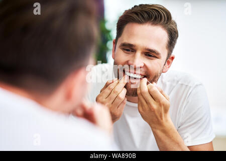 Adult man flossing teeth in the bathroom Stock Photo