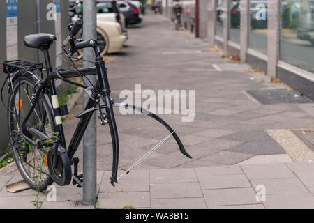 Bike or bicycle lock on steel pole on sidewalk was stolen its front wheel. Stolen wheel bicycle. Abandon vintage bicycle leave on street in Europe. Stock Photo