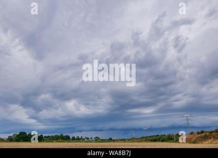 Beautiful dramatic stormy sky and cloud over meadow and high Voltage tower before sunset. Yellow light with sun rays of cumulonimbus cloudscape. Stock Photo