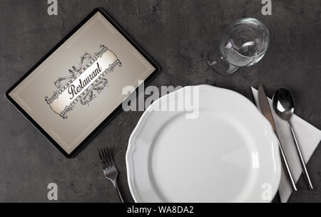 Tablet with stylish restaurant logo and laid table Stock Photo