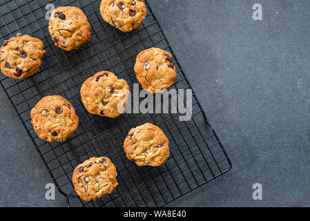 Freshly baked homemade chocolate chip cookies with fruit and nuts, cranberries and almonds, cooling on wire rack, dark background flat lay Stock Photo
