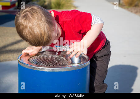 A little boy drinks from a water fountain while playing at a playground Stock Photo