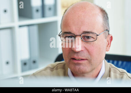 Face of pensive intelligent mature software engineer in glasses checking programming code on computer screen Stock Photo