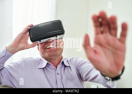 Laughing mature man enjoying playing videogame in virtual reality goggles at home Stock Photo