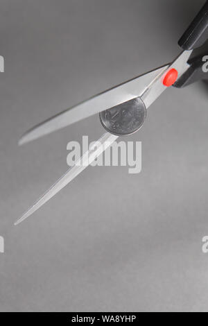 Indian two rupee coin cutting with pair of scissors representing concept 'Cost Cutting' Stock Photo