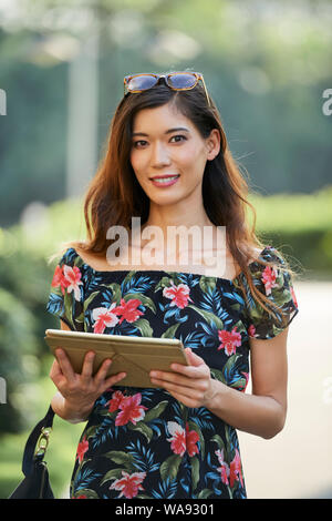 Lovely smiling Japanese brunette using application on tablet computer when walking in park Stock Photo