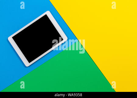 Digital tablet computer on light blue, green and yellow background. Top view Stock Photo