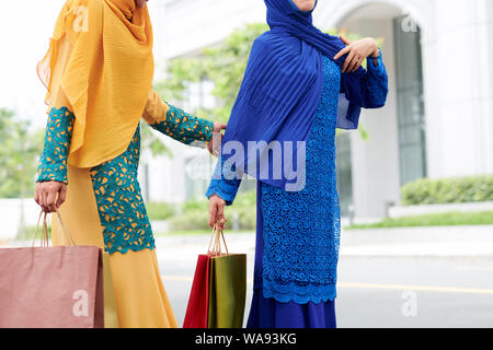 Cropped image of muslim women in bright dresses and hijabs walking in the street with paper-bags after shopping Stock Photo
