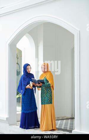 Smiling pretty muslim women in traditional dresses reading holy quaran together Stock Photo