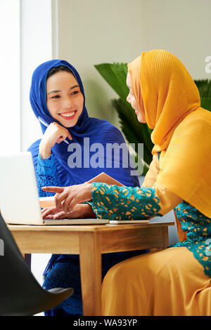 Young pretty Asian muslim woman smiles while typing notes on laptop in ...
