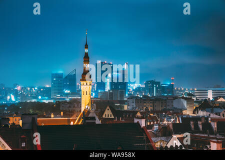 Tallinn, Estonia. Tower Of Town Hall On Background With Modern Urban Skyscrapers. Night City Centre Architecture. Stock Photo