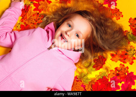 Top view of a happy little girl lying on autumn leaves. Stock Photo