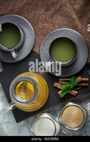 Transparent glass teapot with chitrus tea and cups, tea set on a wooden table. Close up, gray background, soft light. Stock Photo